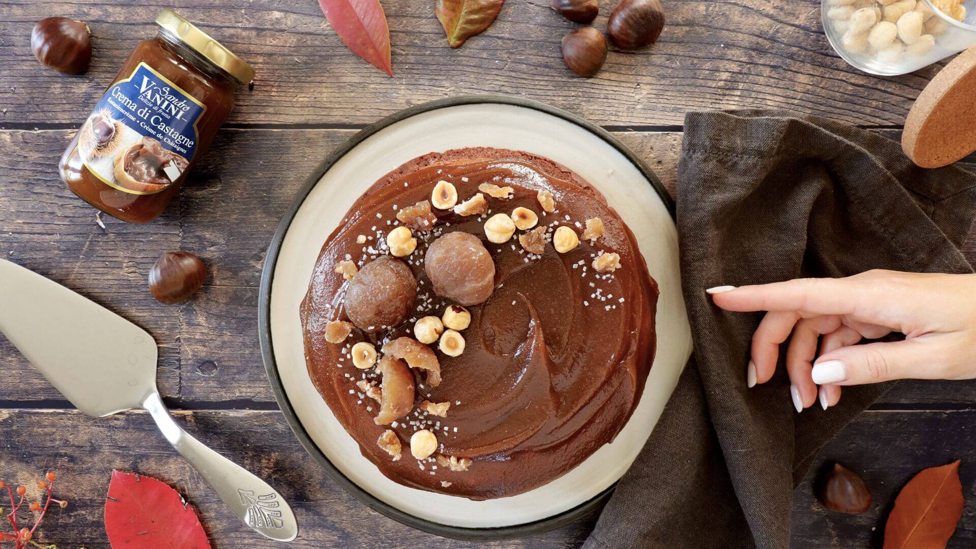 Torta soufflé al cacao decorata con crema di castagne Sandro Vanini, marrons glacés e nocciole croccanti, servita su piatto autunnale.